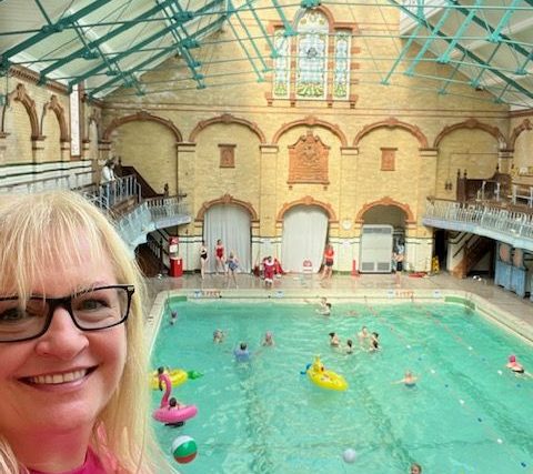 A white woman standing in front of an ornate heritage building, with terracotta and yellow tiles and scrolled metalwork