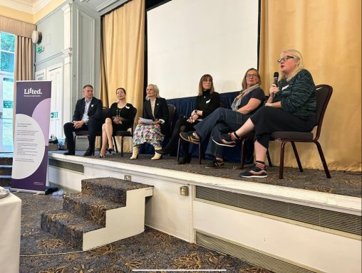 Six people sitting on chairs on a stage talking to a conference