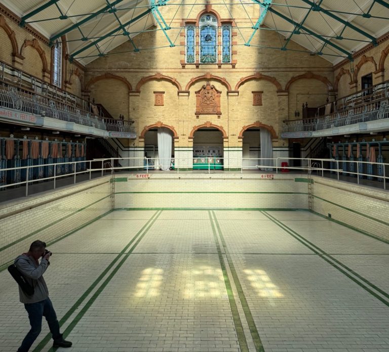 A heritage building with ornate ironwork, tiled empty swimming pool and a photographer taking a picture of the light flooding the pool